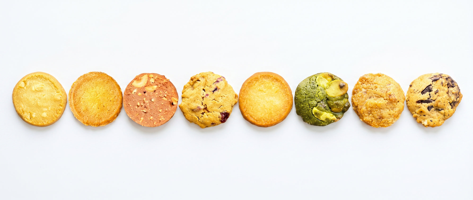 さまざまな種類の焼き菓子を並べたクッキーアソートイメージ。抹茶、チョコチップ、ナッツ、ベリーなど多彩なフレーバーのクッキーをシンプルな背景で表現した商品ビジュアル。