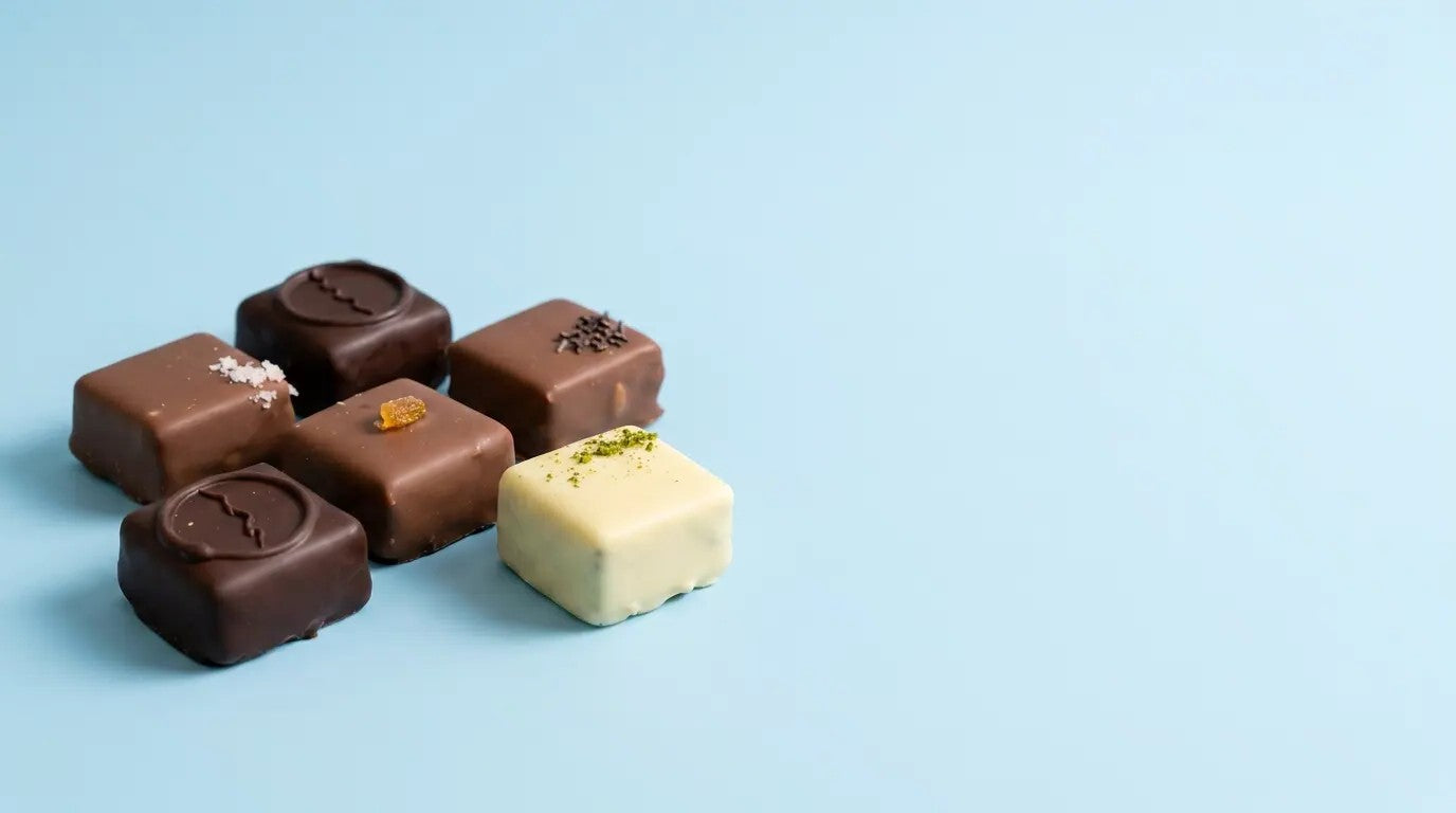 シンプルなブルー背景に並べたボンボンショコラのビジュアル。異なるフレーバーのチョコレートを上品に配置し、高級感と繊細な味わいを表現したショコラ商品イメージ。